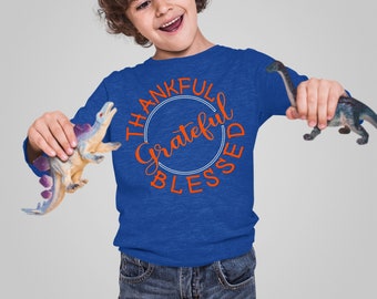 May include: A young person wearing a royal blue long-sleeved shirt with the text "Thankful Grateful Blessed" in a circle on the front. The person is holding two toy dinosaurs.