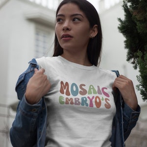 Puede incluir: Una camiseta blanca con el texto "MOSAIC EMBRYO'S" en letras estilizadas de colores.