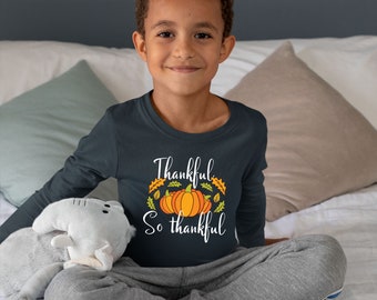 May include: A young person wearing a dark blue long-sleeved shirt with a white graphic of pumpkins and leaves. The shirt says "Thankful So thankful".