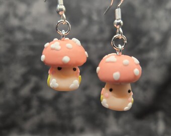 May include: A pair of mushroom-shaped earrings. Each earring features a peach-colored cap with white spots and a cream-colored base. The earrings are suspended from silver-colored fish hook ear wires.