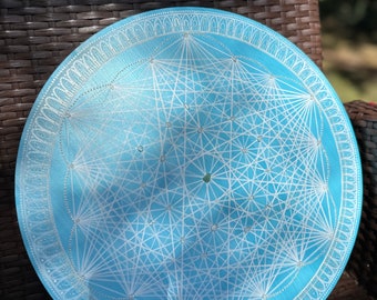 May include: A light blue round plate with a white geometric design. The plate has a decorative border with a repeating pattern.