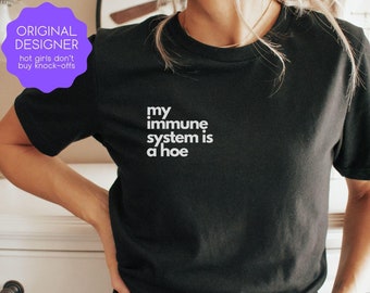 May include: Black t-shirt with the text "my immune system is a hoe" in white. The shirt also has a purple sticker that says "ORIGINAL DESIGNER hot girls don't buy knock-offs".