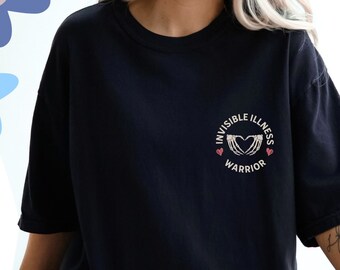 Puede incluir: Camiseta negra con un gráfico de un corazón rodeado de manos esqueléticas. El gráfico está rodeado de un círculo con el texto "Invisible Illness Warrior".