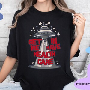 May include: A black t-shirt with a graphic of a UFO and the text "Get in we have health care".