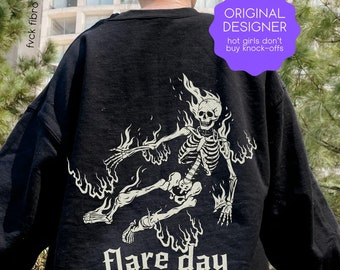 May include: Black sweatshirt with a white graphic print of a skeleton on fire. The text "Flare Day" is printed below the graphic. The text "Original Designer" is printed on a purple circle with the text "hot girls don't buy knock-offs" printed below it.