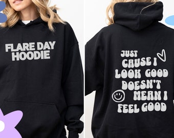 Puede incluir: Sudadera con capucha negra con texto blanco. La parte delantera dice "Flare Day Hoodie". La parte trasera dice "Just Cause I Look Good Doesn't Mean I Feel Good" con una carita sonriente y un corazón.