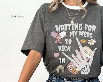 May include: Gray t-shirt with a graphic print of a pill, a skeleton hand, and the text "Waiting for my meds to kick in".