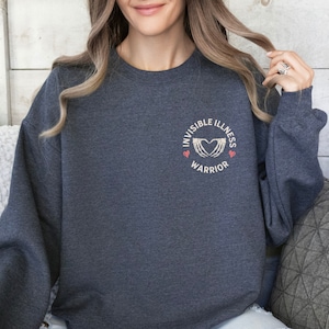 May include: A dark gray sweatshirt with a white graphic on the front that says "Invisible Illness Warrior" with a heart and two hands forming a heart shape.