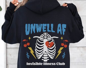 May include: Navy blue hoodie with the text "UNWELL AF" in blue, a white rib cage design with a broken red heart, cherries, stars, lightning bolts, and dollar signs. The text "Invisible Illness Club" is below the graphic.