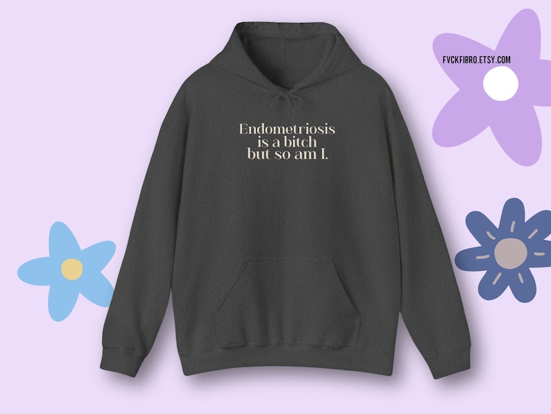 May include: Dark gray hoodie with a front pocket and drawstring hood. The text "Endometriosis is a bitch but so am I." is printed in white. The Etsy shop name FYCKFIBRO.ETSY.COM is in the upper right corner.