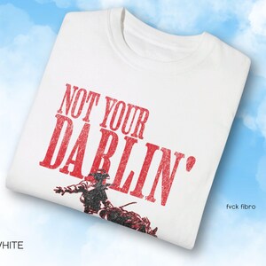 Puede incluir: Camiseta blanca con texto rojo que dice "Not Your Darlin'" y una ilustraci&oacute;n en blanco y negro de un vaquero montando a caballo.