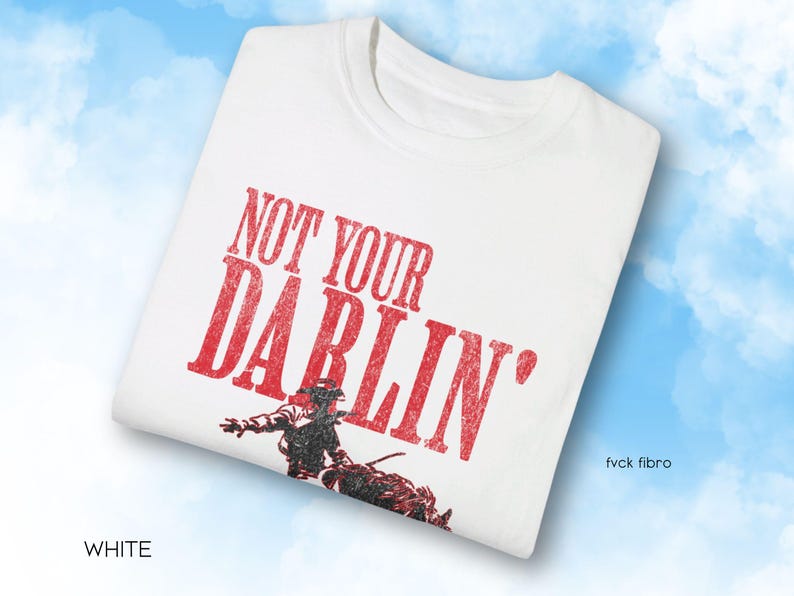 Puede incluir: Camiseta blanca con texto rojo que dice "Not Your Darlin'" y una ilustraci&oacute;n en blanco y negro de un vaquero montando a caballo.