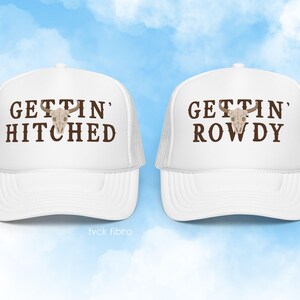 K&ouml;nnte beinhalten: Zwei wei&szlig;e Trucker-Caps mit braunem Text und einem Totenkopf-Motiv. Der Text auf der linken Kappe lautet "Gettin' Hitched" und der Text auf der rechten Kappe lautet "Gettin' Rowdy".