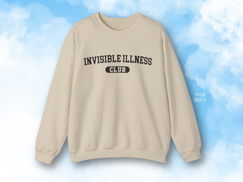 May include: A beige sweatshirt with the text "Invisible Illness Club" printed on the front in black.