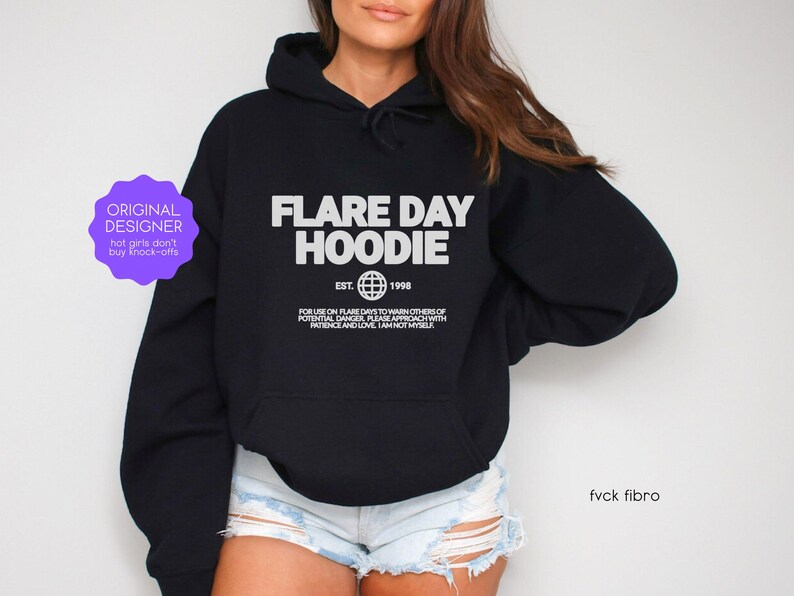 May include: Black hoodie with the text "FLARE DAY HOODIE" in white, along with "EST. 1998" and a globe graphic. The hoodie also has additional text below the main design. The image includes a purple sticker that says "ORIGINAL DESIGNER".
