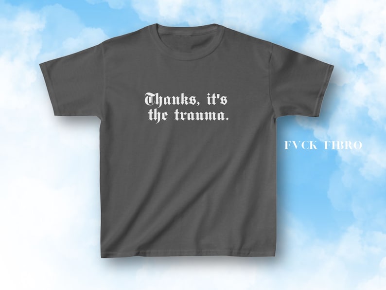 Pu&ograve; includere: Una maglietta grigia scura con il testo "Thanks, it's the trauma." stampato in bianco sul davanti. Il testo &egrave; in font gotico. La maglietta ha un collo rotondo e maniche corte.