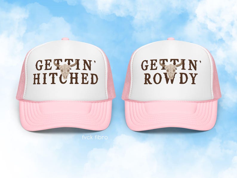 K&ouml;nnte beinhalten: Zwei rosafarbene Trucker-Caps mit wei&szlig;en Netzr&uuml;cken. Die linke Kappe tr&auml;gt die Aufschrift "Gettin' Hitched" und die rechte Kappe die Aufschrift "Gettin' Rowdy". Beide Kappen zeigen einen braunen Sch&auml;del mit H&ouml;rnern.