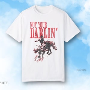 Puede incluir: Camiseta blanca con un gr&aacute;fico rojo de una persona montando a caballo. El gr&aacute;fico dice "Not Your Darlin'" en rojo.
