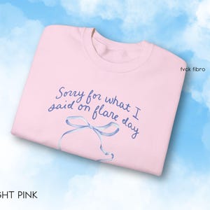 May include: Light pink sweatshirt with the text "Sorry for what I said on flare day" in blue lettering and a blue ribbon illustration.