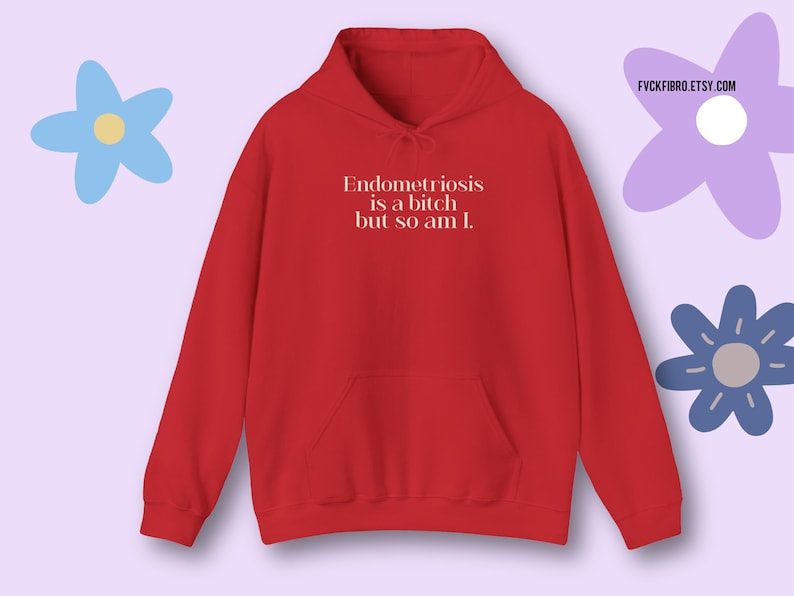 May include: Red hoodie with the text "Endometriosis is a bitch but so am I." The hoodie has a front pocket and a drawstring hood. The Etsy shop URL "FYCKFIBRO.ETSY.COM" is visible. The background includes blue and purple flower illustrations.
