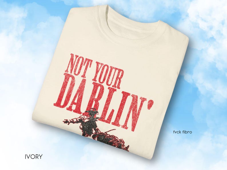 Puede incluir: Una camiseta blanca con el texto "NOT YOUR DARLIN'" en letras rojas. Debajo del texto se ve un vaquero montando un caballo.