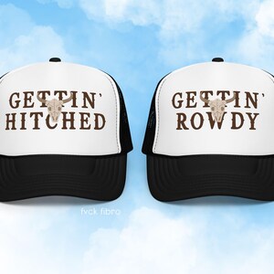 K&ouml;nnte beinhalten: Zwei schwarze und wei&szlig;e Trucker-Caps mit einem Totenkopf-Motiv und dem Text "Gettin' Hitched" und "Gettin' Rowdy" in brauner Schrift.