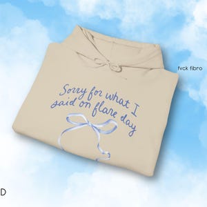 May include: A beige hoodie with the text "Sorry for what I said on flare day" in blue cursive writing. A blue ribbon is drawn on the hoodie.