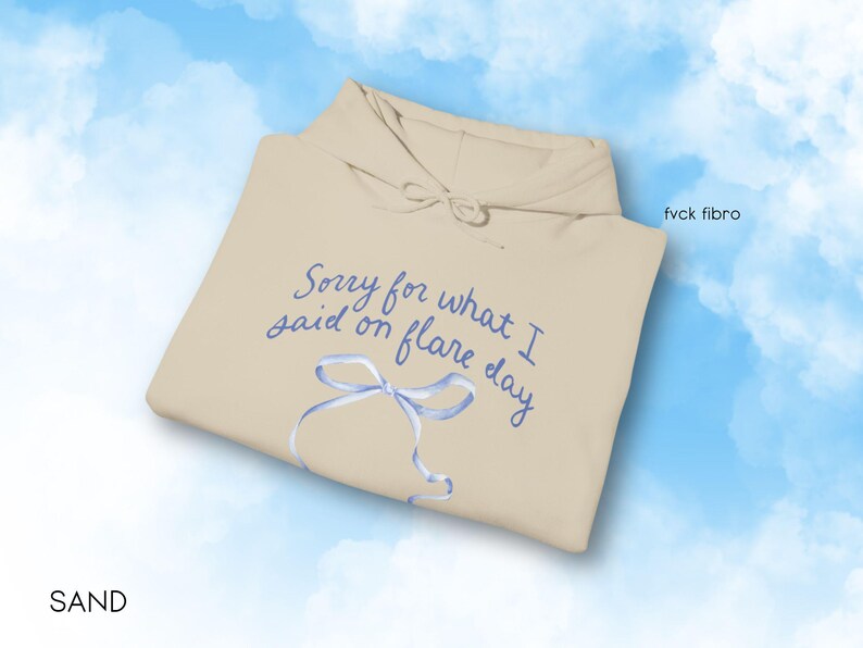 May include: A beige hoodie with the text "Sorry for what I said on flare day" in blue cursive writing. A blue ribbon is drawn on the hoodie.