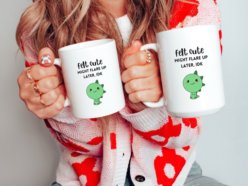 Pu&ograve; includere: Due tazze in ceramica bianca con un motivo di dinosauro verde e il testo "felt cute might flare up later, idk".
