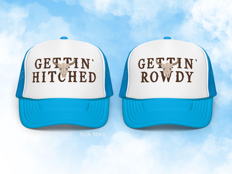 K&ouml;nnte beinhalten: Zwei wei&szlig;e Trucker-Caps mit blauen Netzr&uuml;cken. Eine M&uuml;tze sagt "Gettin' Hitched" und die andere "Gettin' Rowdy". Beide M&uuml;tzen zeigen einen braunen Sch&auml;del mit H&ouml;rnern.