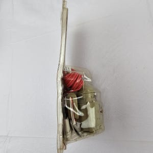 May include: A vintage olive green toy milk can with a red rope, packaged in a clear plastic blister pack. The packaging is attached to a white cardboard backing. The toy is likely from the mid-20th century.