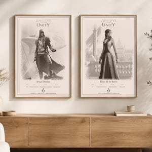 Op de afbeelding: Twee ingelijste wandposters met personages uit Assassin's Creed Unity. De linker poster toont Arno Dorian met de tekst 'Liberty, Equality, Brotherhood'. De rechter poster toont Elise de la Serre met de tekst 'Duty, Endurance, Resolve'.