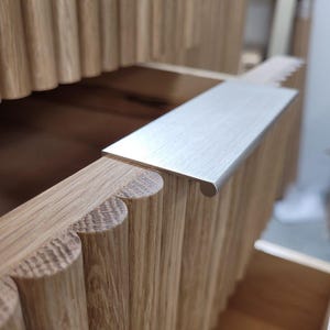 May include: Close-up of a wooden drawer with a silver metal pull handle. The drawer front is made of vertical wooden slats.