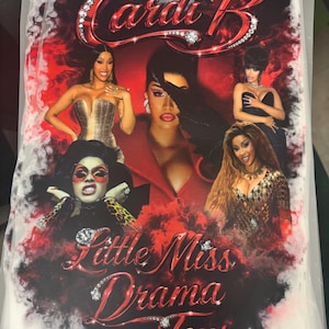 Peut inclure: Graphique avec plusieurs images de Cardi B, avec le texte "Cardi B" dans une police ornée de bijoux en haut. En dessous, le texte "Little Miss Drama Tour" est affiché dans une police similaire ornée de bijoux. Le fond est un mélange de rouge et de noir.