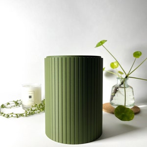 May include: A green cylindrical container with vertical grooves. The container is made of a smooth, matte material and has a simple, modern design.