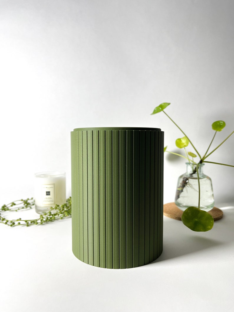 May include: A green cylindrical container with vertical grooves. The container is made of a smooth, matte material and has a simple, modern design.