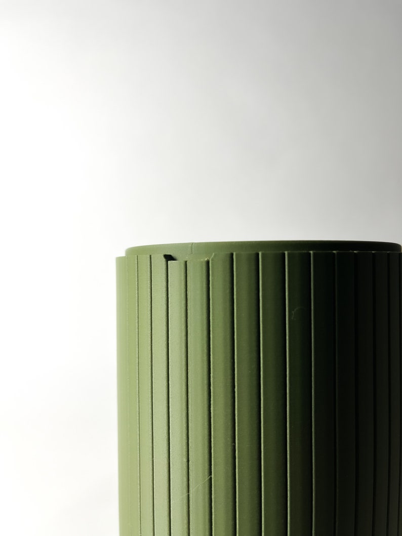 May include: A green cylindrical container with vertical grooves. The container is made of a smooth, plastic-like material.