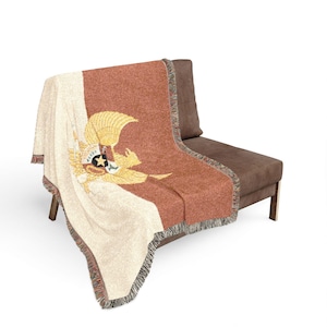 Peut inclure: Un plaid tissé présentant un design divisé en crème et orange terre cuite. Le centre affiche un emblème d'aigle doré détaillé avec un bouclier contenant une étoile noire et des rayures. Les bords sont finis avec un détail de franges décoratives.