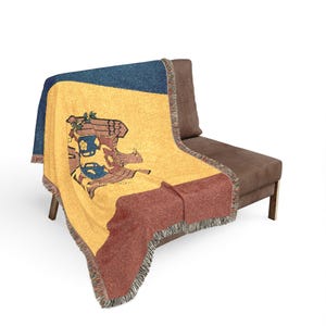 May include: A woven throw blanket featuring the vertical tricolor design of the Moldova flag in blue, yellow, and red. The centre of the yellow section displays the national coat of arms, which includes an eagle holding a cross and a shield.