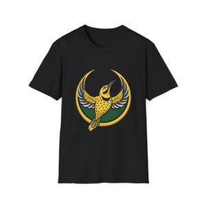 May include: Black t-shirt featuring a yellow bird with black and white wings, and a yellow body with black spots. The bird is set against a green and gold crescent moon design. The shirt is made of a soft material.