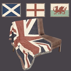 May include: A woven throw blanket featuring the Union Jack flag draped over a brown chair. Above it are three smaller rectangular woven blankets displaying the flags of Scotland, England, and Wales, each with a fringed edge and textured finish.