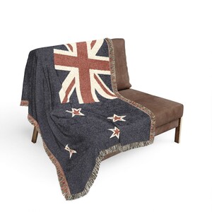 May include: A woven throw blanket featuring a dark charcoal grey background with a prominent Union Jack design in cream and muted red. The blanket includes four five-pointed stars in cream and red, finished with a decorative fringed edge.