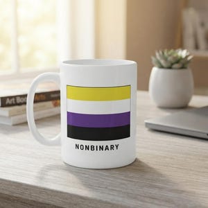 May include: A white ceramic mug featuring a rectangular graphic of the nonbinary pride flag, which consists of horizontal yellow, white, purple, and black stripes. The word NONBINARY is printed in black capital letters directly below the flag.
