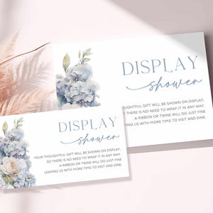 May include: Two white cards with blue text and floral watercolor designs. The cards read "DISPLAY shower" in elegant script. One card has a larger floral arrangement of blue hydrangeas.