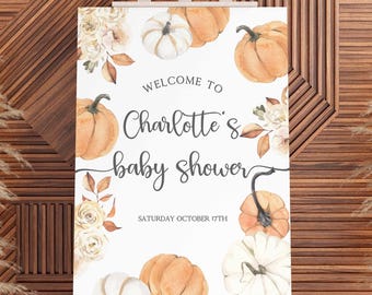 Op de afbeelding: Een babyborrelbord op een ezel. Het bord toont aquarel pompoenen en bloemaccenten. De tekst luidt "Welkom bij Charlotte's babyborrel" en "Zaterdag 17 oktober". De achtergrond is een houten muur.