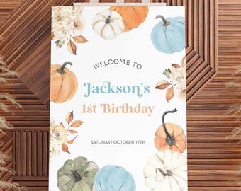 May include: A birthday welcome sign for Jackson's first birthday, with watercolour pumpkins in orange, white, green, and blue. The sign includes floral accents and the date, Saturday, October 17th. The sign is displayed on a wooden easel.