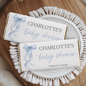 May include: Two white chocolate bar wrappers with blue ribbon designs. The text on the wrappers reads "Charlotte's baby shower" and "Thanks for coming!"