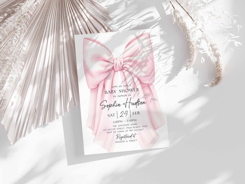 Op de afbeelding: Een babyborrel uitnodiging met een grote, aquarel roze strik. De uitnodiging bevat de tekst "Join us for a Baby Shower in Honor of Sophia Hudson" en evenement details. Het ontwerp staat op een witte achtergrond met zachte schaduwen.
