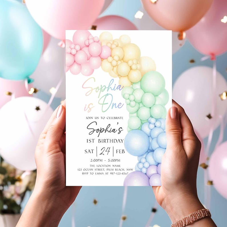 May include: A pastel-colored birthday invitation held by hands, featuring a rainbow balloon arch design. The invitation reads "Sophia is One" and includes event details: date, time, and location. Balloons in various pastel shades fill the background.