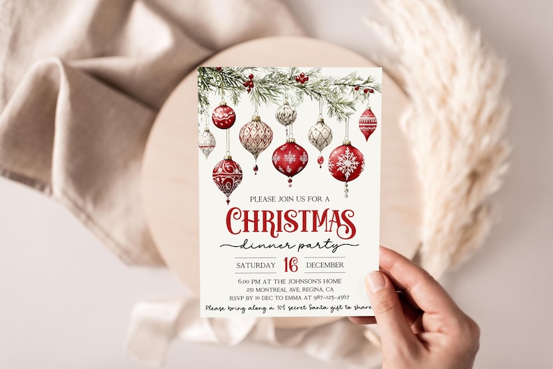 May include: A Christmas dinner party invitation with a red and white color scheme. The invitation features a watercolor illustration of red and white ornaments hanging from a pine branch. The text reads "Please join us for a Christmas dinner party, Saturday 16 December, 6:00 PM at the Johnson's Home, 25 Montreal Ave, Regina, CA, RSVP by 10 Dec to Emma at 97-123-4567, Please bring along a $10 secret Santa gift to share."